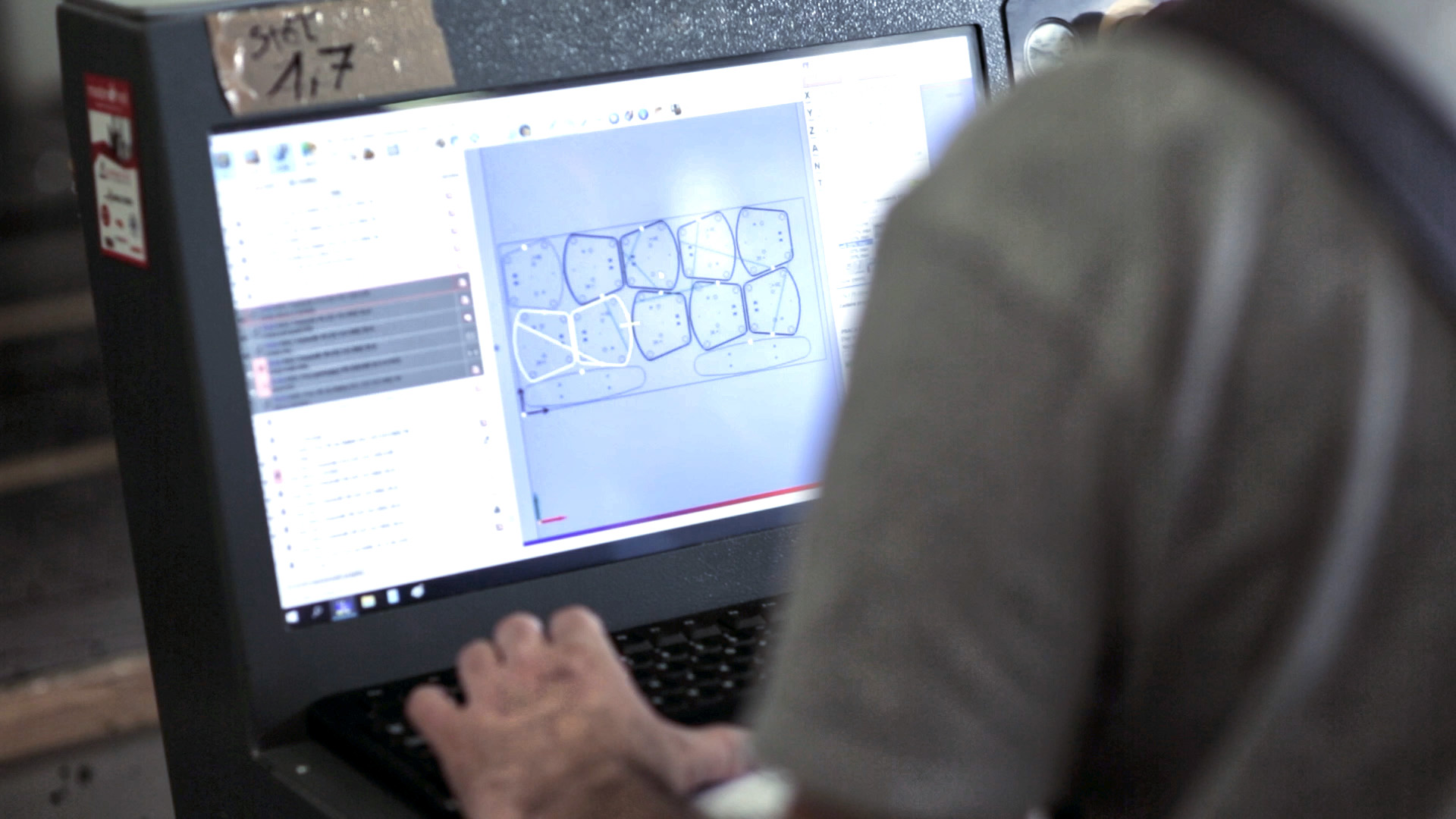An operator at the control panel of a CNC machine, with a digital nesting layout of parts to be cut on the screen