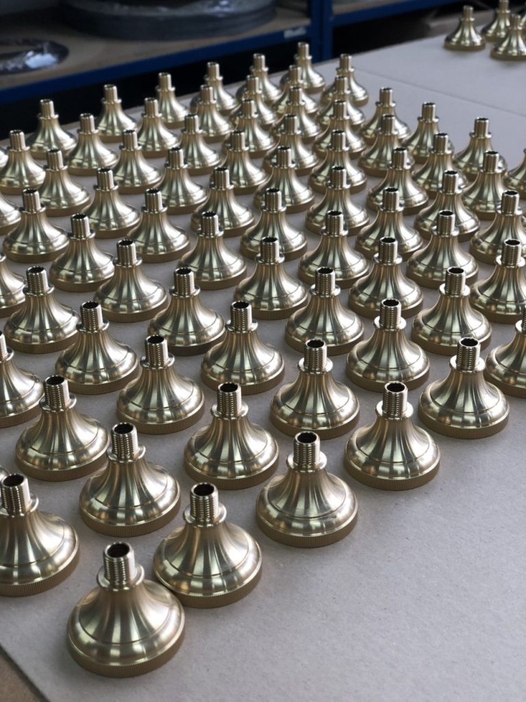 Brass turned conical components with threads, arranged in neat rows on a workshop bench.