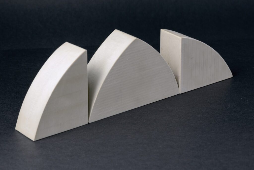 Three beige plastic components with curved wedge profiles lined up in a row on a dark background.