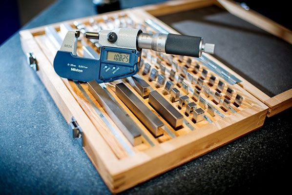 A digital micrometer lying on an open wooden case with a set of precision steel gauge blocks.