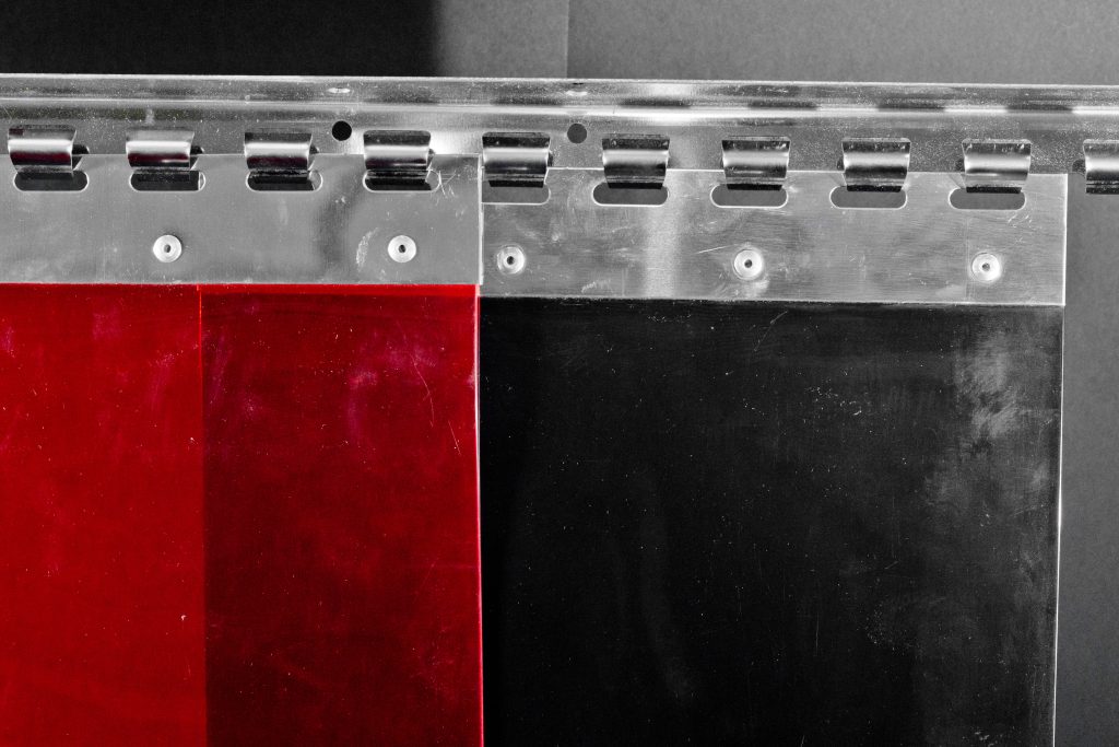 Three PVC curtain strips - dark red welding red and blackout black on a hook rail