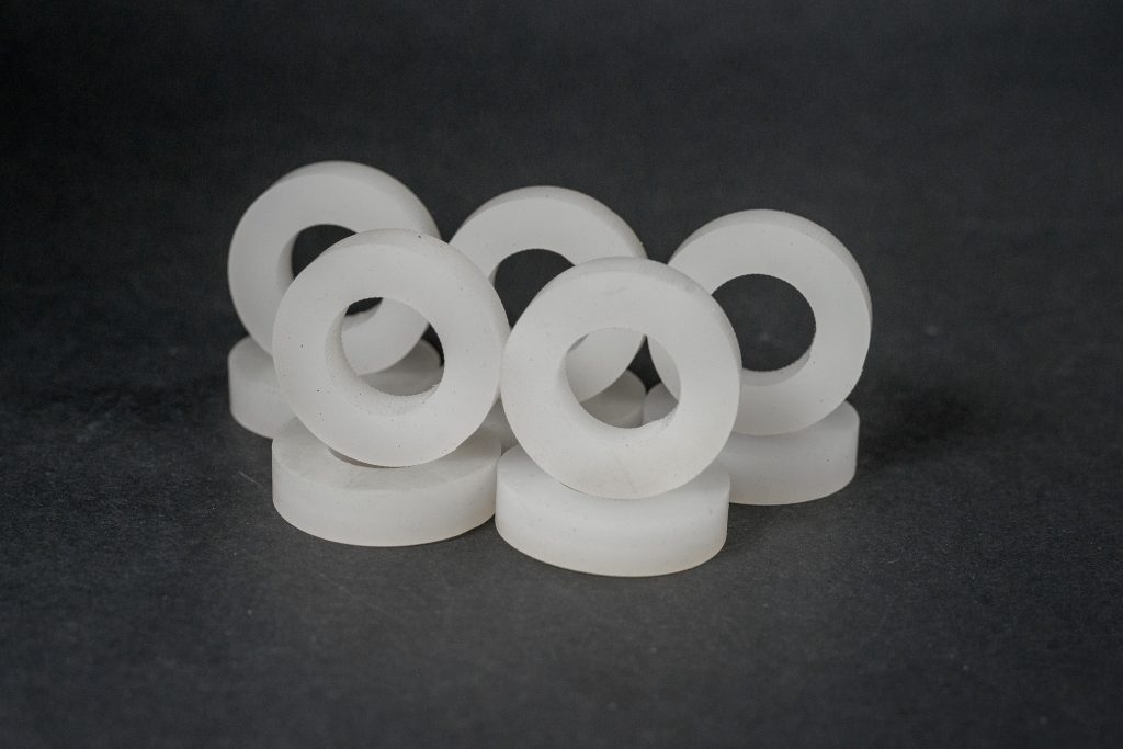 A group of turned white plastic rings with central holes standing on a dark surface.
