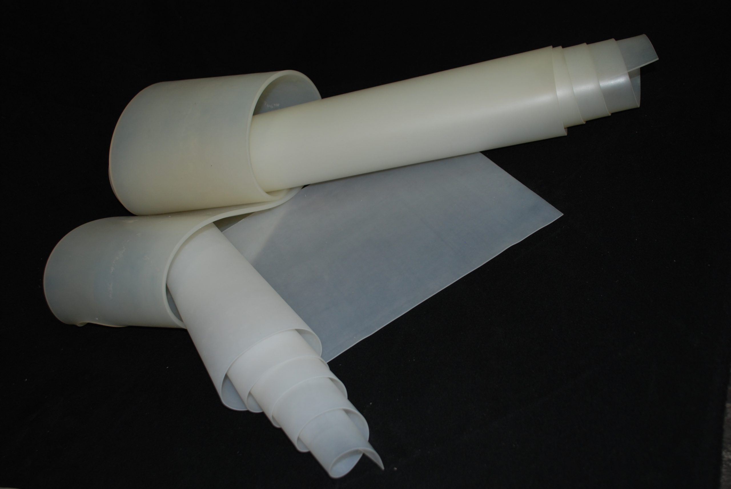 Two rolled-up flexible sheets of milky colour lying on a background, one of them unrolling into a rectangular sheet.