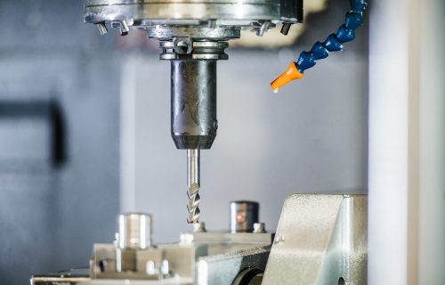 A metal milling cutter mounted in the spindle of a CNC machine tool, with a blue coolant hose beside it.