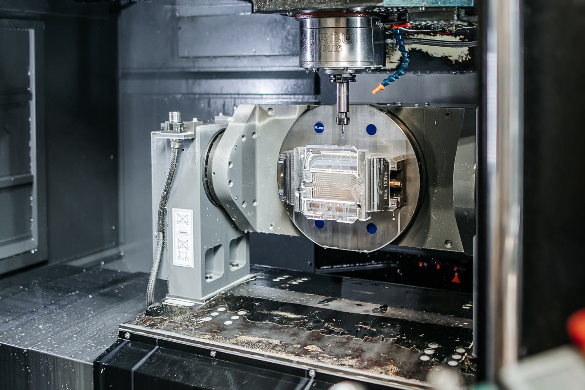 A part clamped in a vice on the rotary table of a CNC milling machine during precision milling of microchannels.