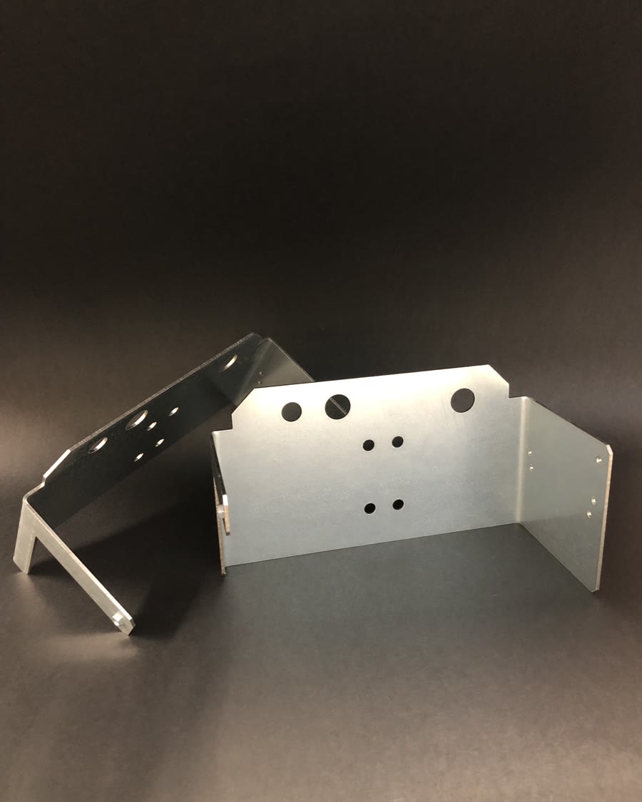 Two silver, bent metal components with numerous holes of various diameters set against a dark background.