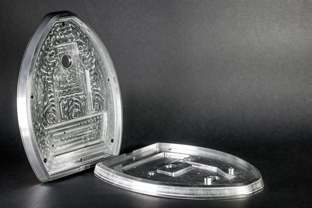 Two precisely milled metal parts with a rounded shape, featuring recesses and holes, arranged against a black background.