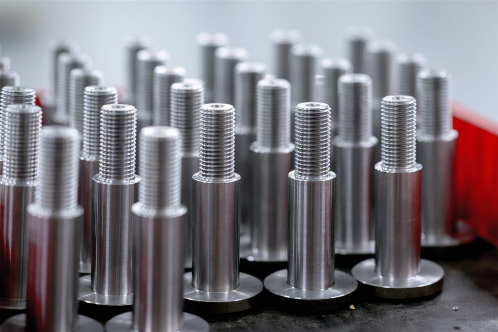 Silver metal pins with a threaded end and a round base, arranged in rows on a dark worktop.