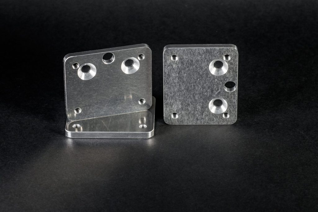 Milled metal plates with a brushed surface and mounting holes, set against a black background.
