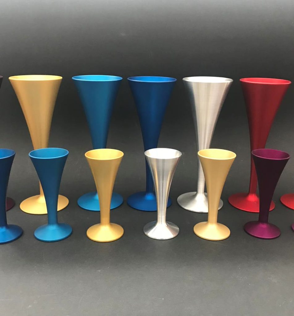 Turned metal cup-shaped components in various colours and sizes, standing against a dark background.