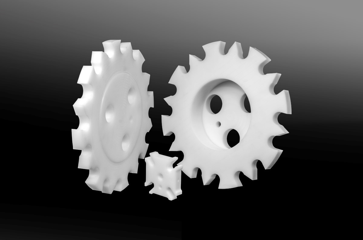 White plastic gears with visible mounting holes, shown against a dark background.
