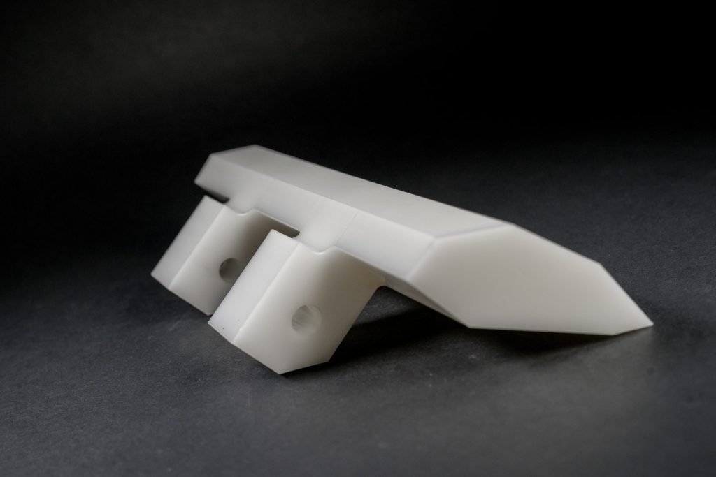 Three white milled plastic parts of irregular shapes arranged against a dark studio background.