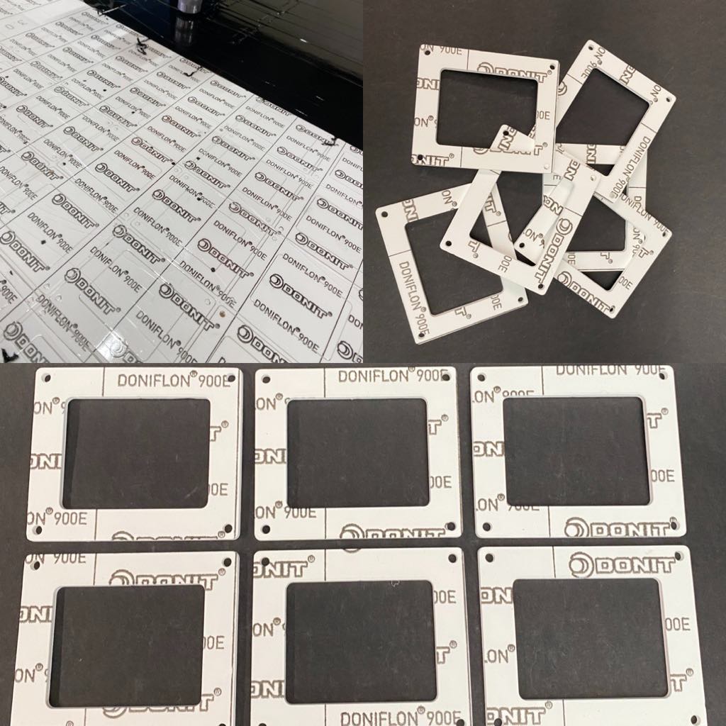 White square flat parts with a central rectangular hole and four small holes in the corners lying on a table.
