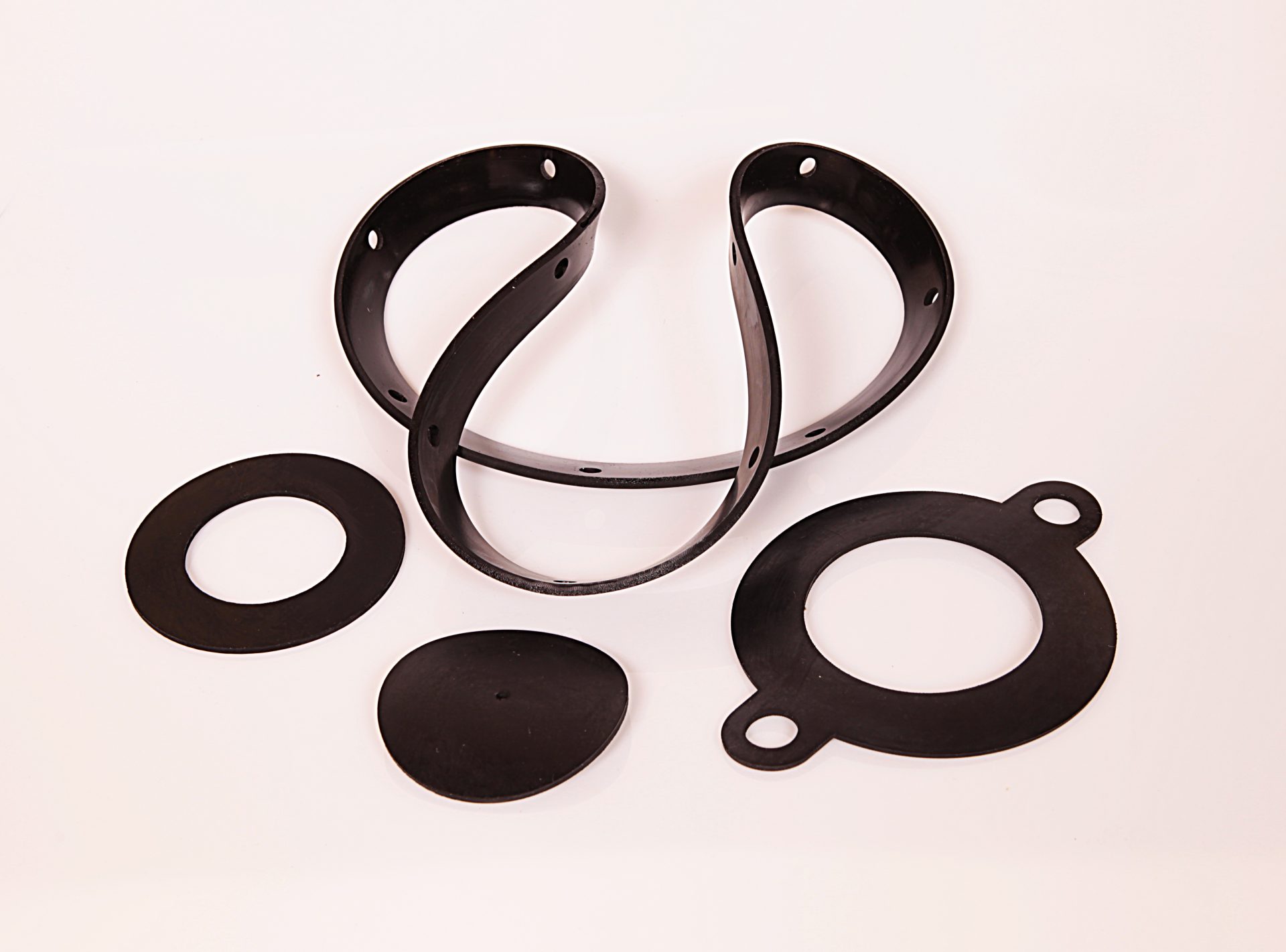 Four black rubber gaskets in various shapes and perforated strips arranged on a white background.