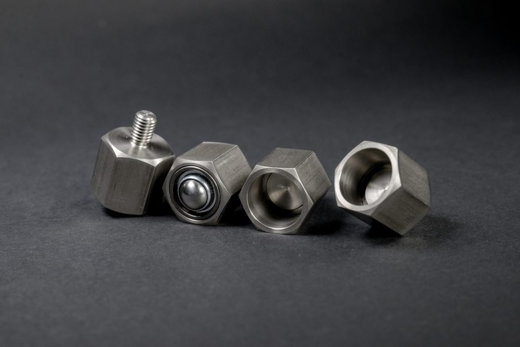 Four silver, brushed metal hexagonal parts arranged in a row against a dark background.