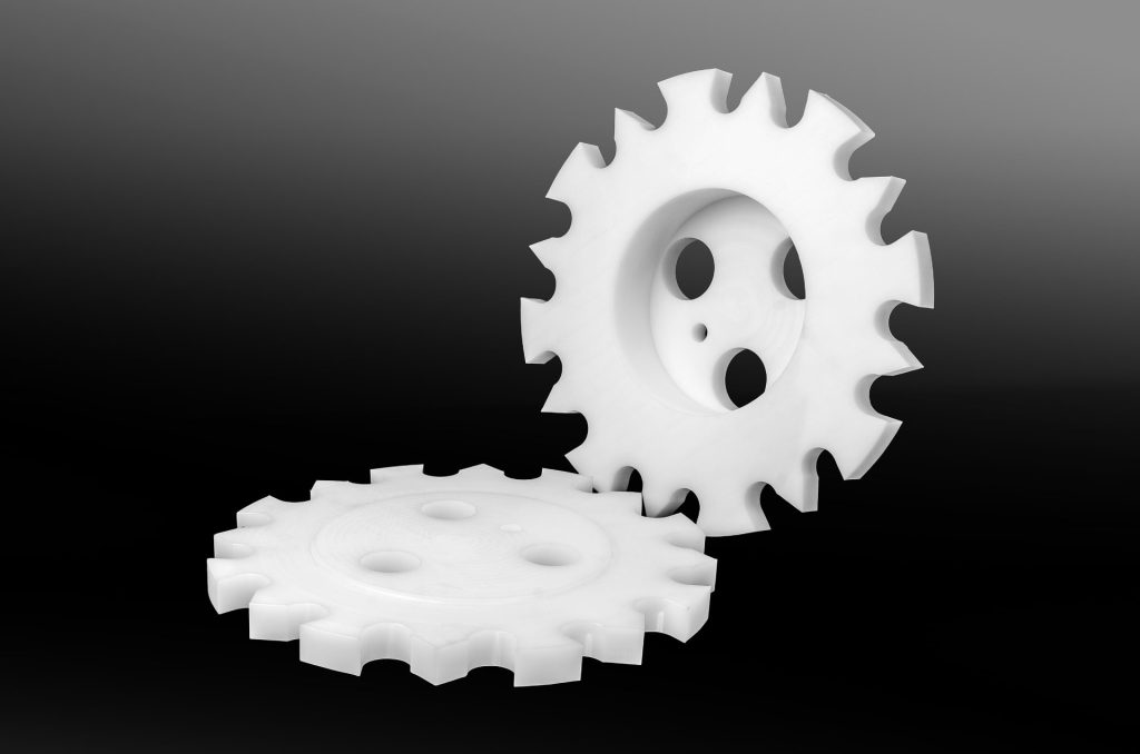 Two white plastic sprockets with holes and evenly spaced teeth on a dark background.