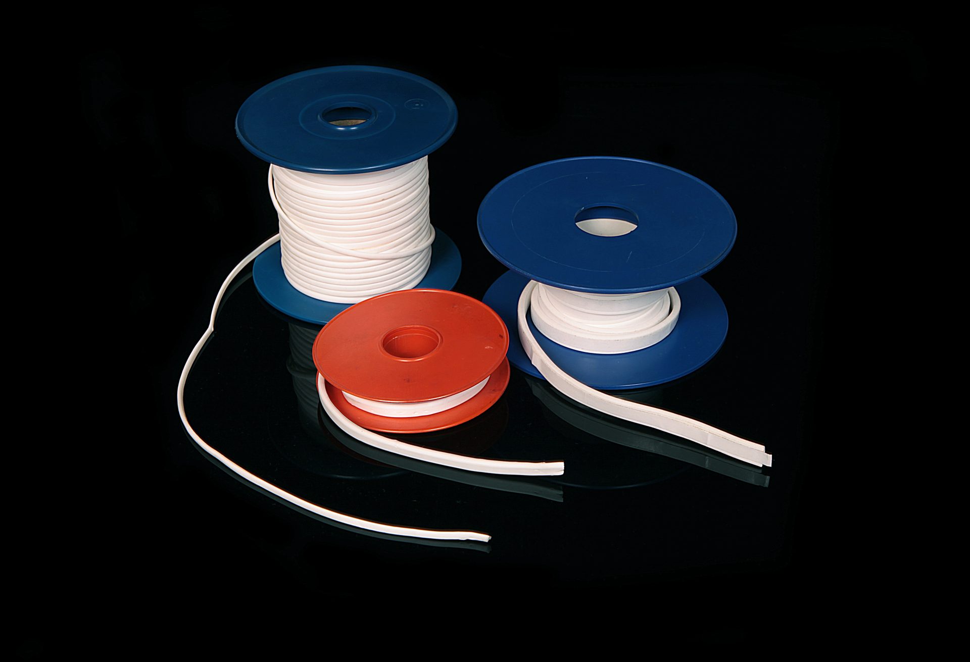 Two blue and one red spool with white sealing tape wound on them, on a black, glossy surface.