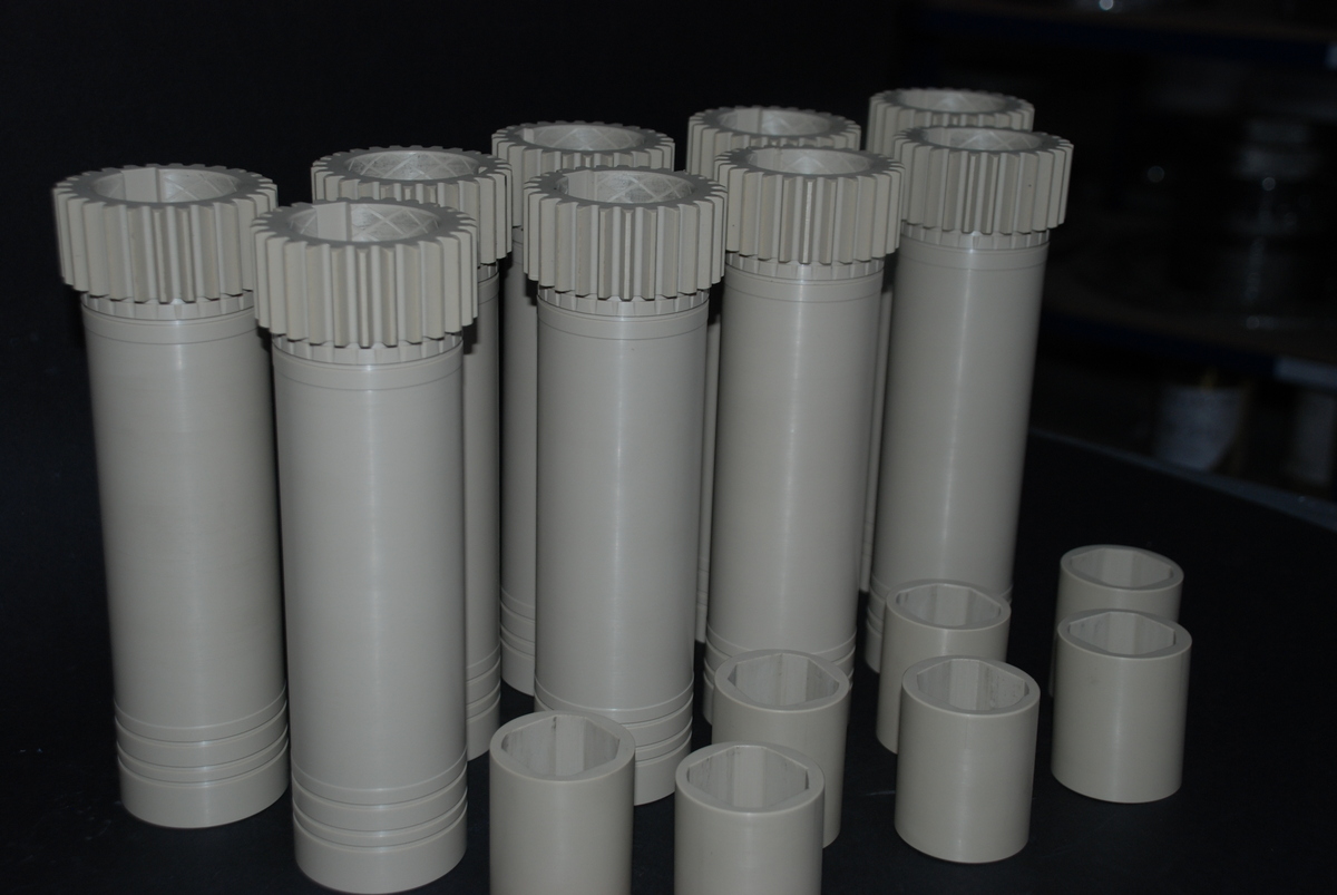 A group of turned cylindrical plastic components with toothed rims, standing on a dark surface.