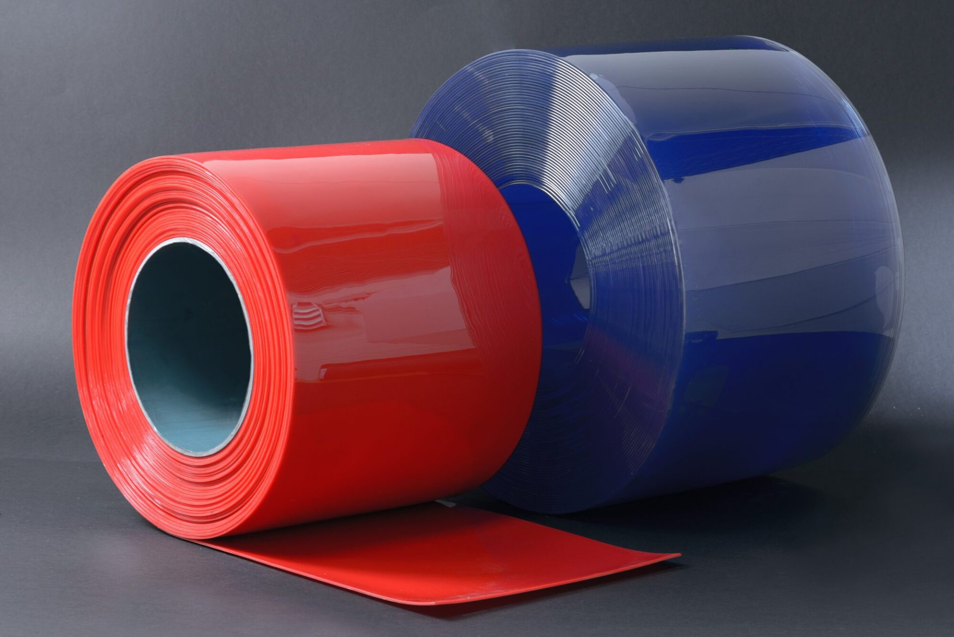 Two glossy rolls of plastic tape: a smaller red one with an unrolled end and a larger blue one, on a grey background.