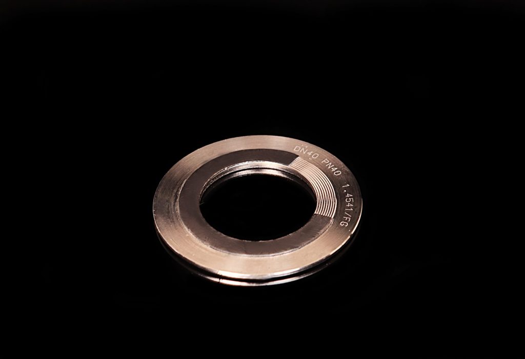 Spiral wound metal gasket with visible technical markings on a black, reflective background.