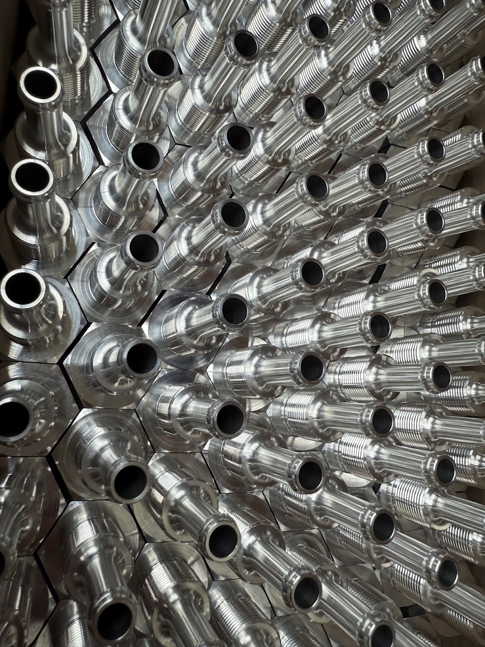 Silvery metal parts of cylindrical shape with visible ribbing and holes, densely arranged side by side.