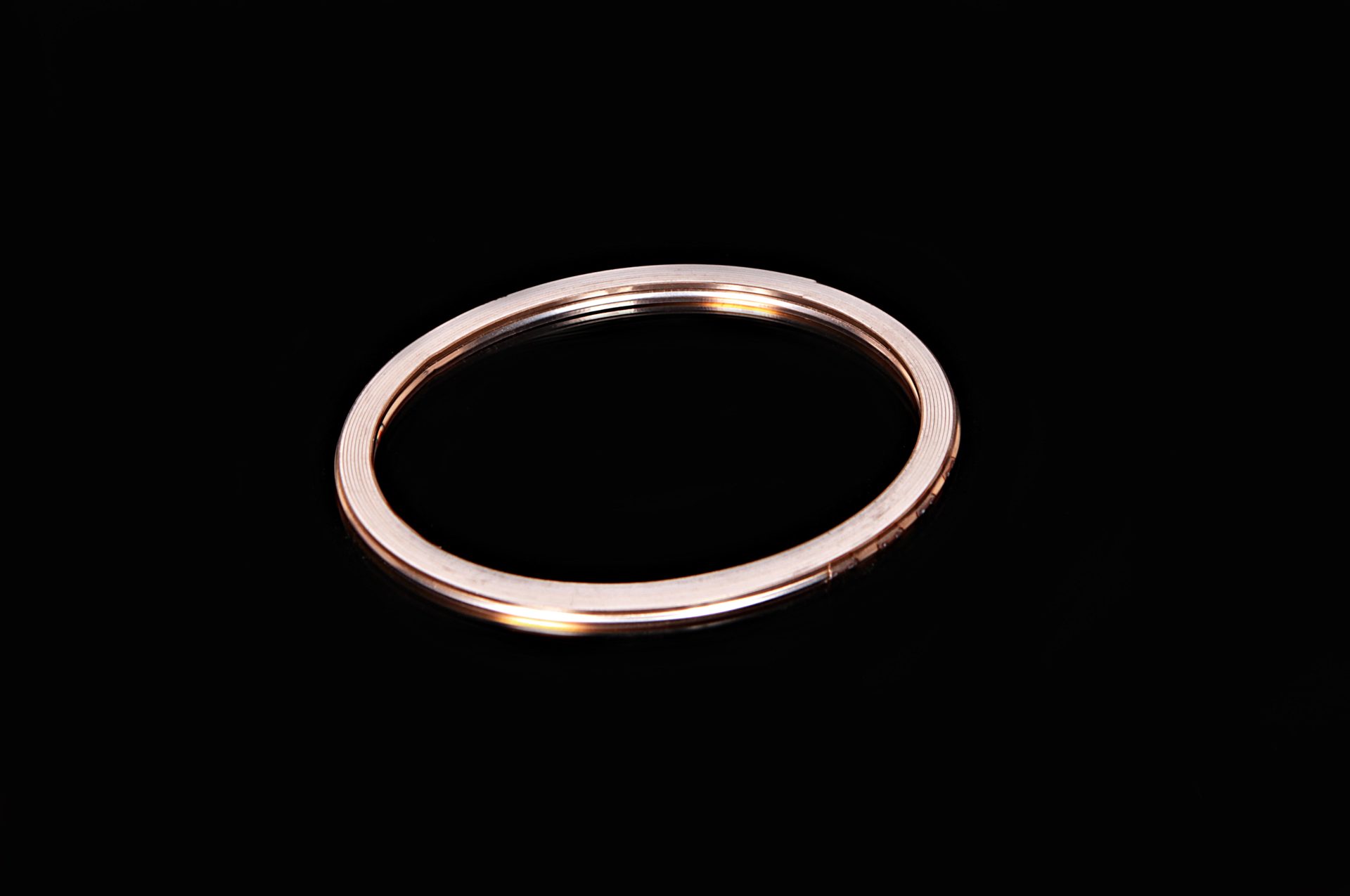 An oval copper gasket with fine grooves on its surface, set against a black background.