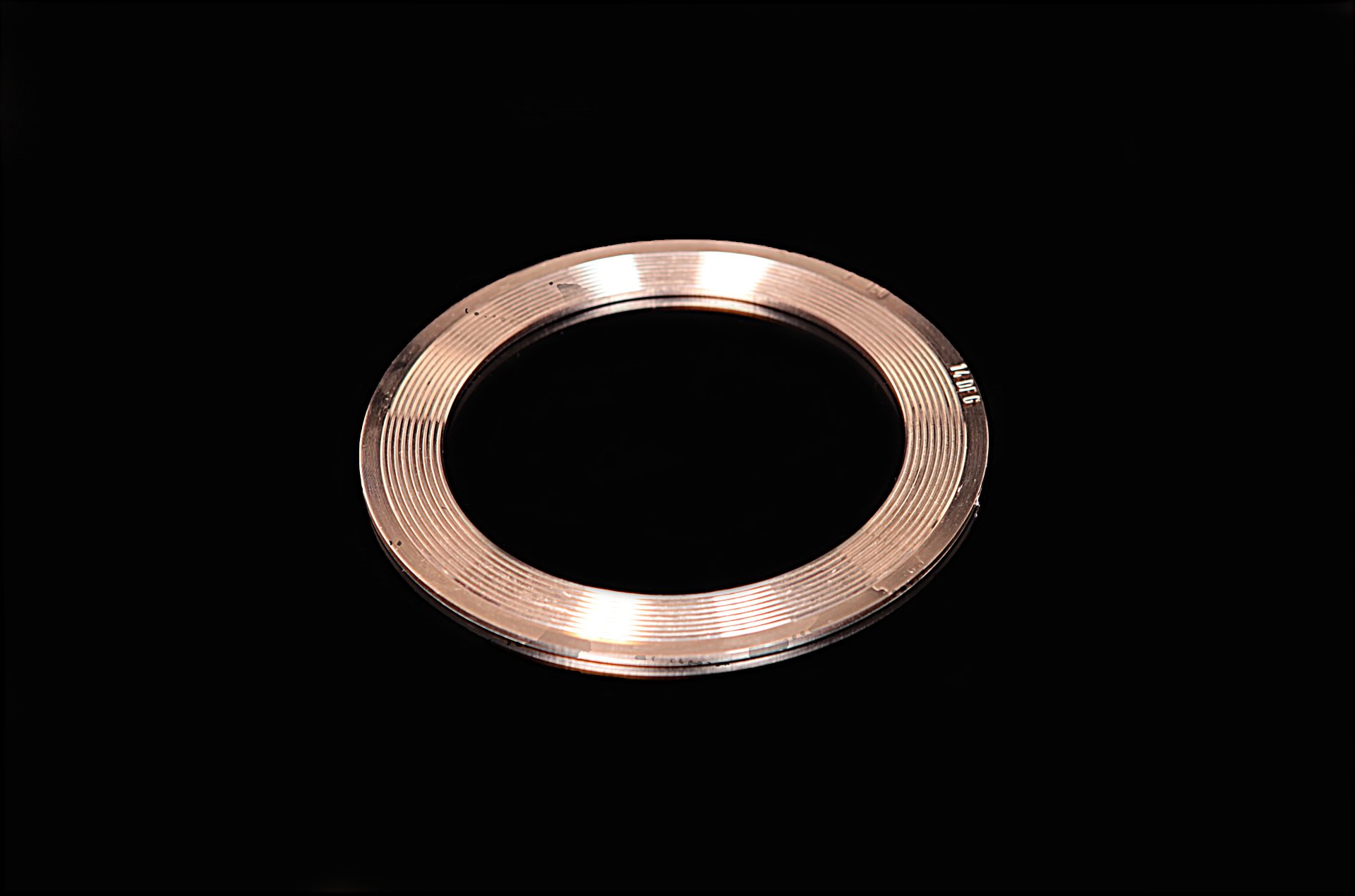 Copper metal ring with a flat surface and numerous grooves, lying on a black background with a visible number.