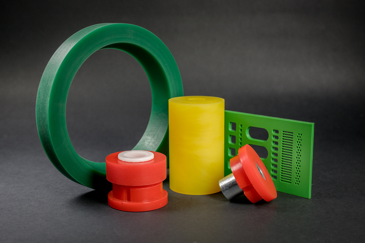 Smooth objects lie on a dark background, including a green ring, a yellow cylinder, a red sleeve and a green plate with holes.