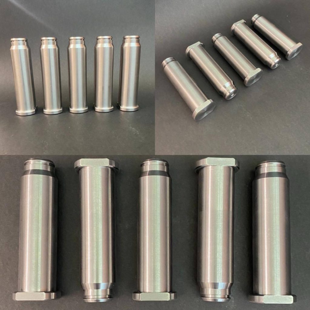 Five cylindrical silver metal components with smooth surfaces, lying at even intervals on a black background.