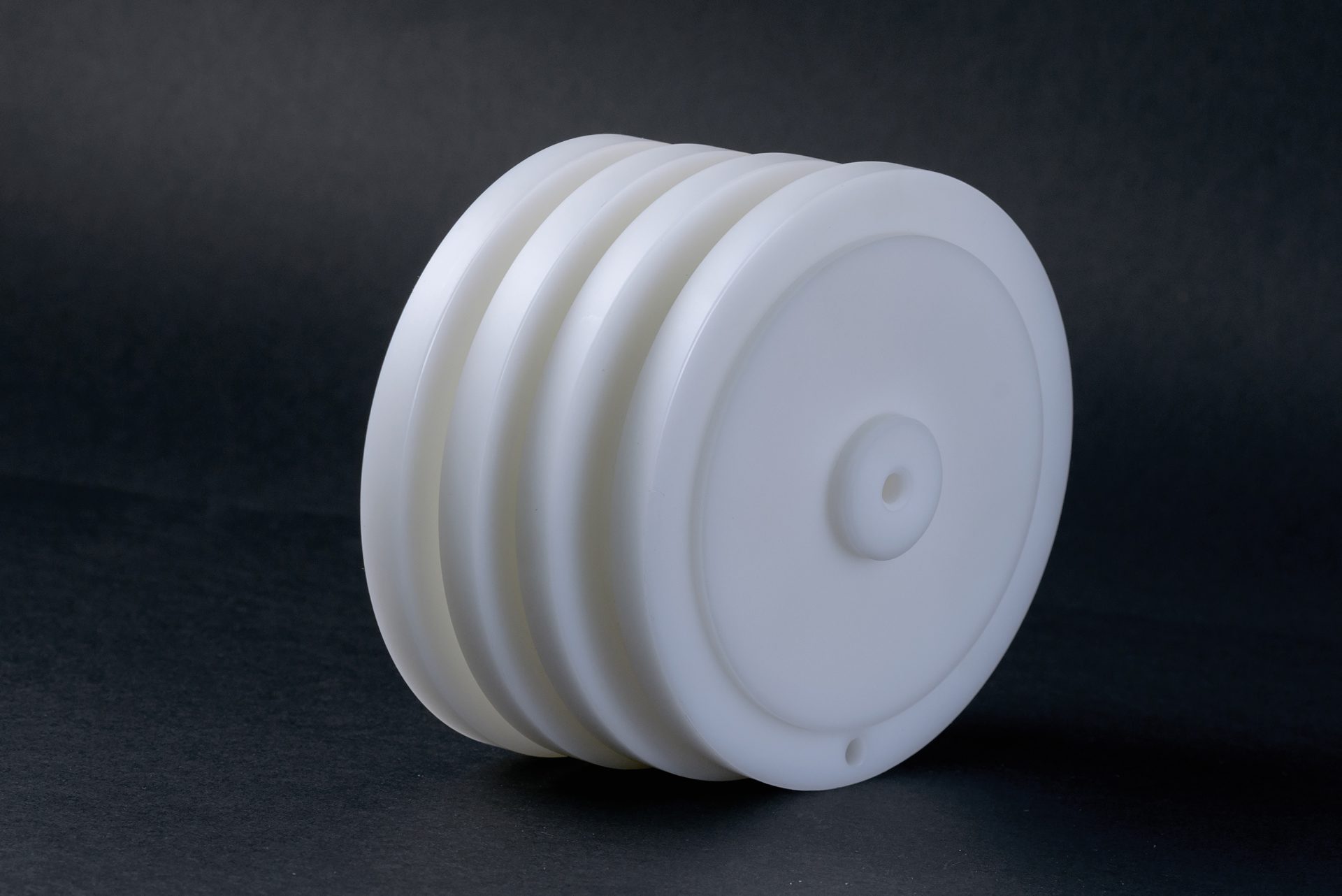 A stack of white plastic pulleys with wide grooves and a central hole against a dark studio background.