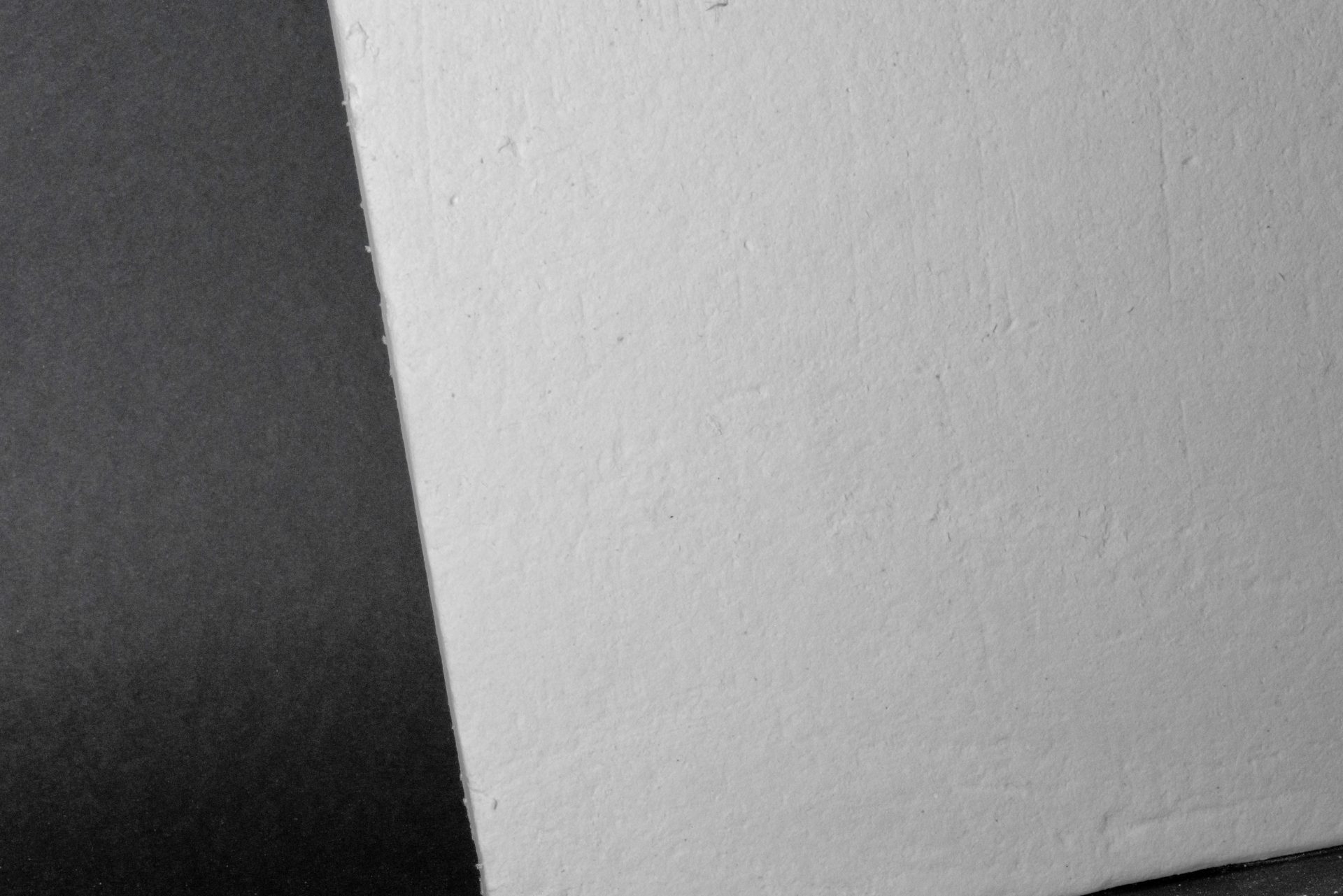 A thick light-grey board with a rough structure placed beside a dark-grey smooth surface in the frame.