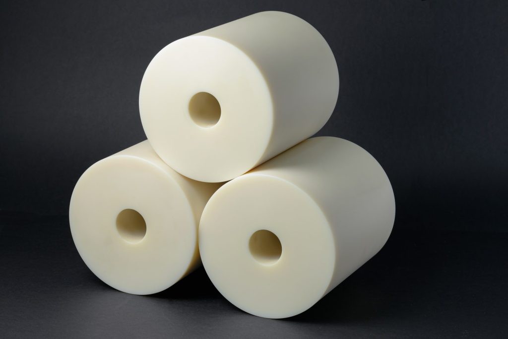 Three cream-coloured plastic cylinders with smooth surfaces and central bores stacked in a pyramid on a dark background.