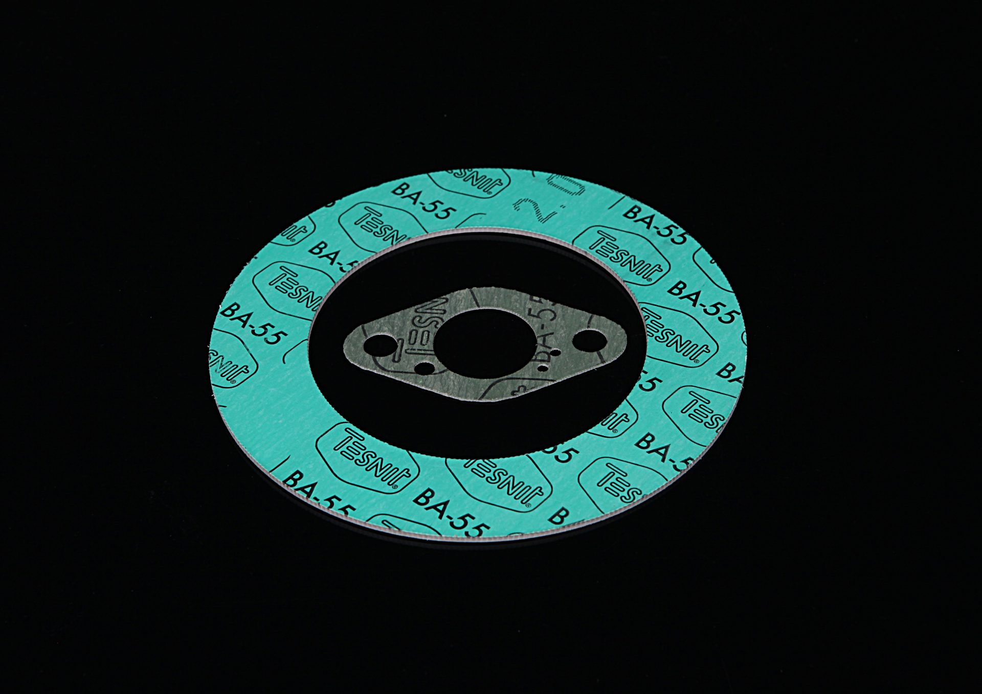 Turquoise flange gasket with a large hole and printed markings, and a smaller metal ring on a black background.