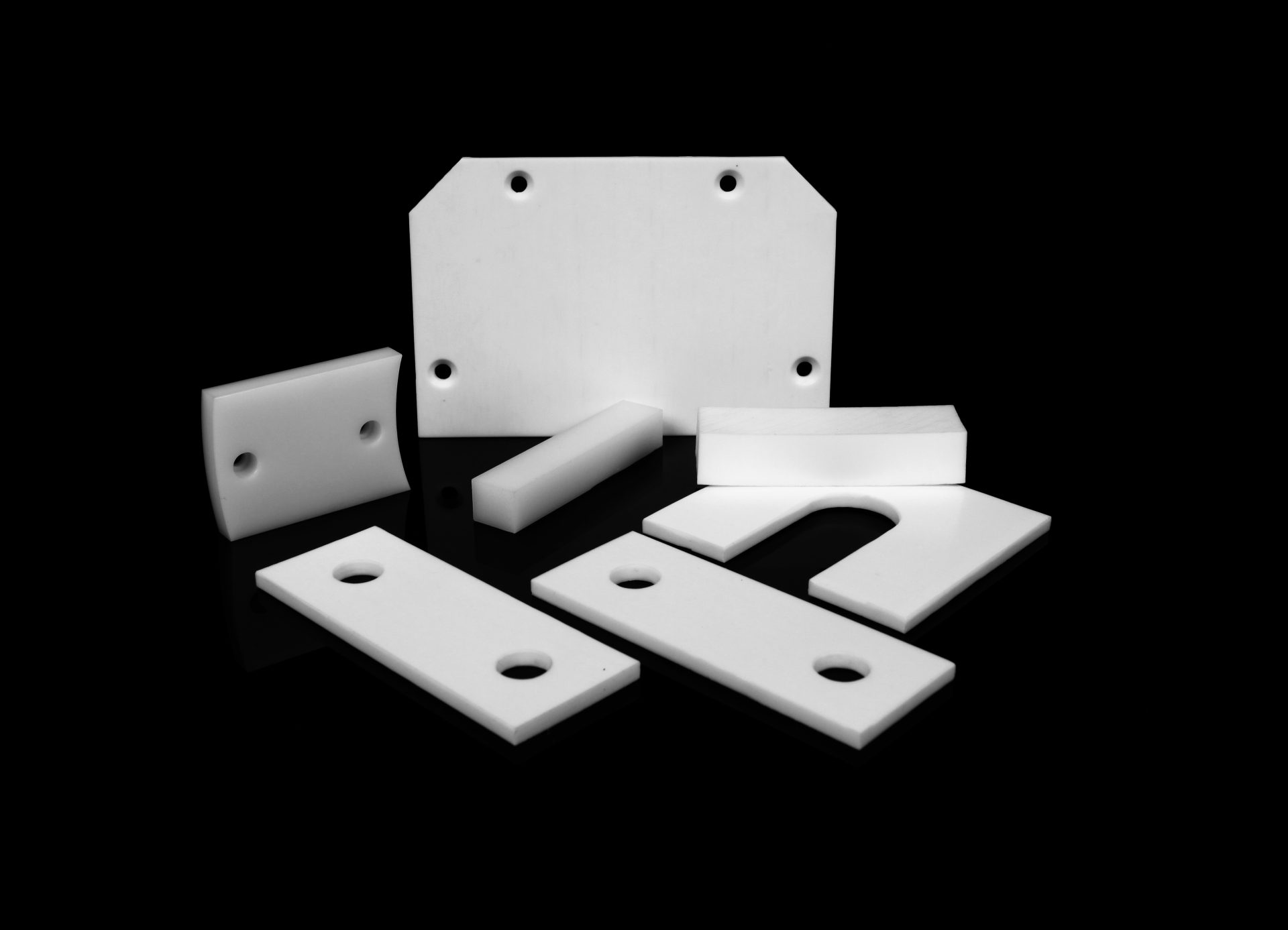 A set of white plastic parts with holes and cut-outs arranged on a black, glossy surface.