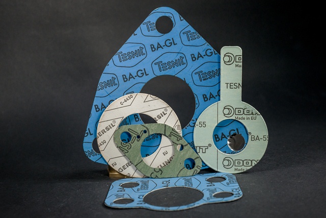 Set of flat technical gaskets in blue, green and white with holes on a dark surface.